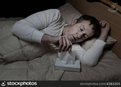 Horizontal image of sick mature man, reaching for tissue, while in bed