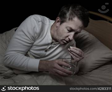 Horizontal image of sick mature man, taking medicine, while in bed