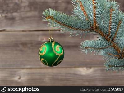 Horizontal image of single Christmas ornament hanging from real Blue Spruce tree branch with rustic wood in background
