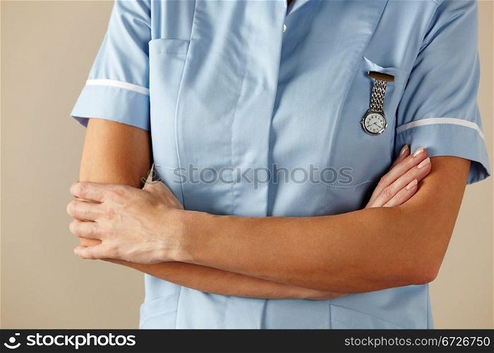 horizontal,indoors,studio shot,white background,nurse,health service,hospital,nhs,medical,healthcare,uniform,blue,standing,arms folded,watch,mid section,people,one person,female,woman,caucasian,adult,30s,thirties,cropped,british,english,uk