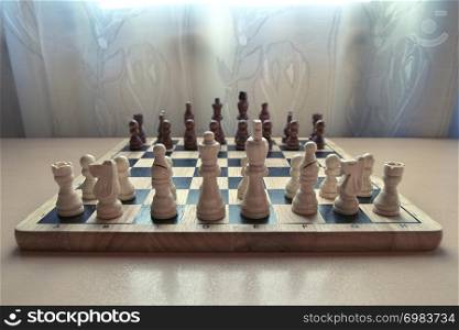 Horizontal low angle view photographic image of a retro style wooden material chessboard with chess pieces set ready for strategic mind game. White colored figures in front. Focus on pawns.
