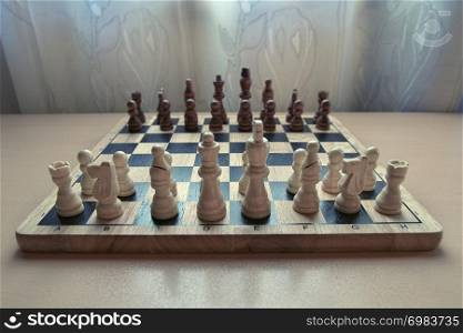 Horizontal low angle view photographic image of a retro style wooden material chessboard with chess pieces set ready for strategic mind game. White colored figures in front. Focus on pawns.