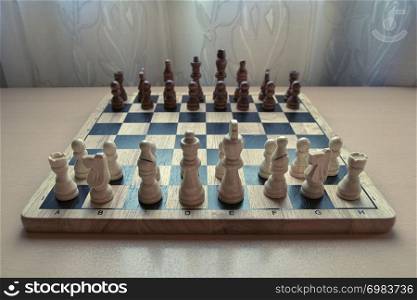 Horizontal low angle view photographic image of a retro style wooden material chessboard with chess pieces set ready for strategic mind game. White colored figures in front.