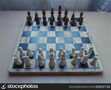 Horizontal low high angle view photographic image of a retro style wooden material chessboard with chess pieces set ready for strategic mind game. White colored figures in front.