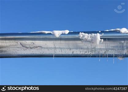 Horizontal metal zinced pipe shining in the sun. Winter picture - the remains of snow and icicles on the pipe surface