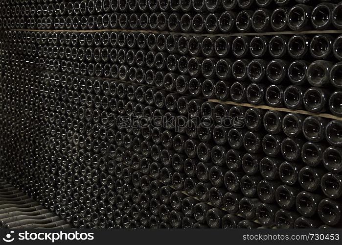 Horizontal perspective view of rows of many champagne bottles in a wine cellar