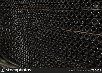Horizontal perspective view of rows of many champagne bottles in a wine cellar