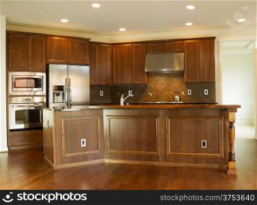 Horizontal photo of a modern residential kitchen with stone counter tops, stainless steel appliances, cherry wood cabinets and hardwood floors