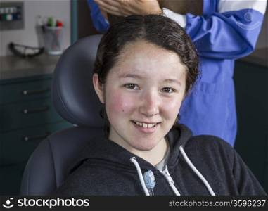 Horizontal photo of a young girl smiling in dentist chair with woman dental assistant behind her