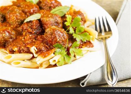 Horizontal photo of bread coated cooked meatballs in pasta with fork, napkin, basil, parsley,and red sauce in round white plate