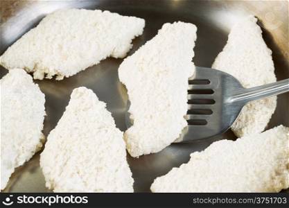 Horizontal photo of breaded coated fish placing place into stainless steel frying pan with focus on single piece with spatula