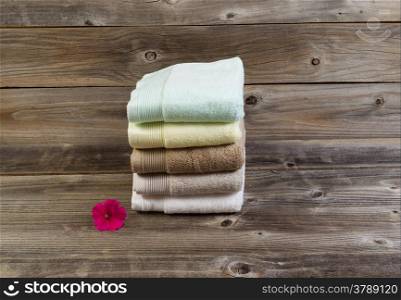 Horizontal photo of clean stacked towels and single healthy flower on rustic wood