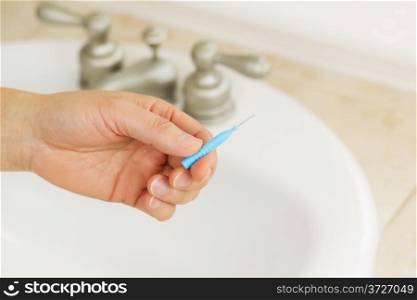 Horizontal photo of female hand holding dental tooth pick in bathroom with sink and counter top in background