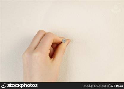 Horizontal photo of female hand holding nail against interior home white wall