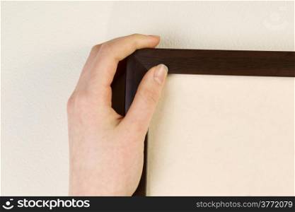 Horizontal photo of female hand holding picture frame against interior home white wall