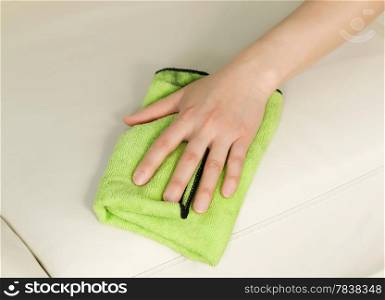 Horizontal photo of female hand wiping white leather sofa with microfiber rag
