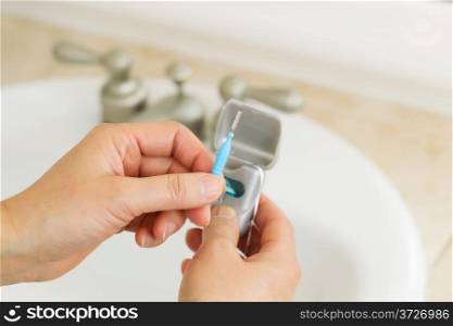 Horizontal photo of female hands holding dental tooth pick in bathroom with dental floss container, sink and counter top in background