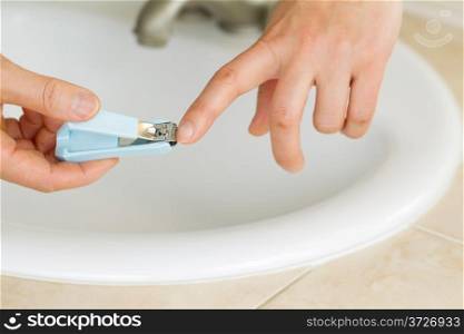 Horizontal photo of female hands trimming fingernails in bathroom with sink and counter top in background