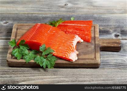 Horizontal photo of fresh raw red salmon fillet on traditional wooden server with parsley on the side and rustic wood underneath