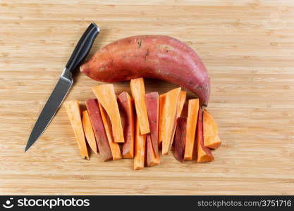 Horizontal photo of freshly cut Yams for cooking French fries with knife and bamboo cutting board