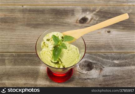 Horizontal photo of green tea ice cream and fresh mint leaf inside of small glass bowl with rustic wood underneath