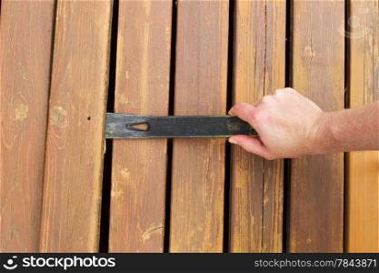 Horizontal photo of hand with pry bar lifting up old cedar wood board on outdoor wooden deck