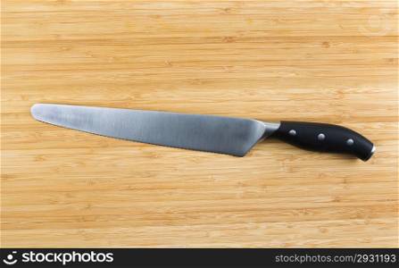 Horizontal photo of large serrated knife on natural bamboo board
