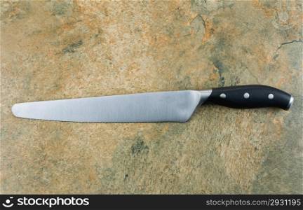 Horizontal photo of large serrated knife on natural stone counter top