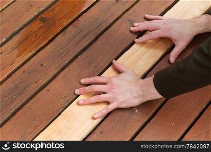 Horizontal photo of male hands putting in a single new cedar wooden board next to fading wood on outdoor deck