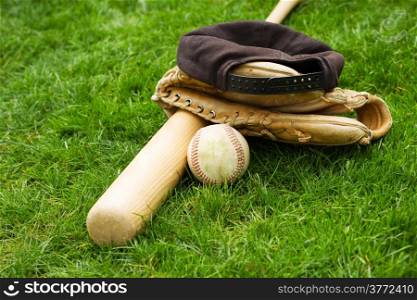 Horizontal photo of old baseball, bat, cap and glove on natural grass field