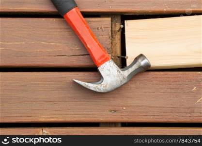 Horizontal photo of old hammer next to aged wood and exposed rusty nails with new cedar board being installed