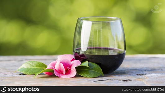 Horizontal photo of red wine in glass and late spring pink flower with bright green background