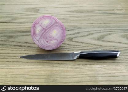 Horizontal photo of sliced purple onion with single knife lying on aged white ash boards