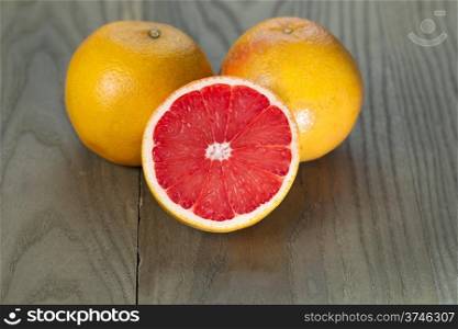 Horizontal photo of sliced ruby red grapefruit half in front of two whole fruits on aged wood&#xA;