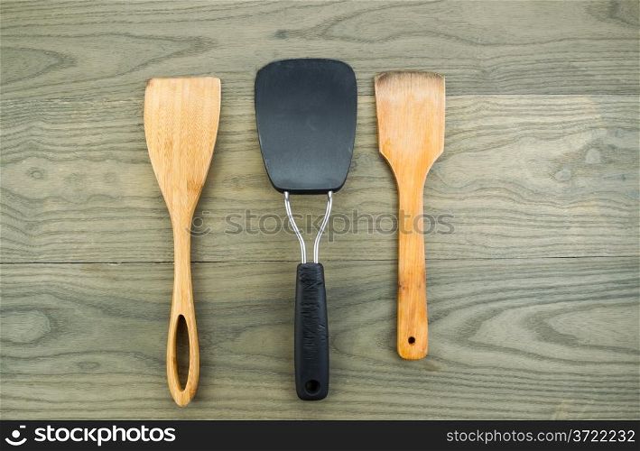 Horizontal photo of three kitchen spatulas, two of them wooden, on aged white oak boards