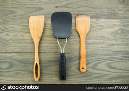 Horizontal photo of three kitchen spatulas, two of them wooden, on aged white oak boards