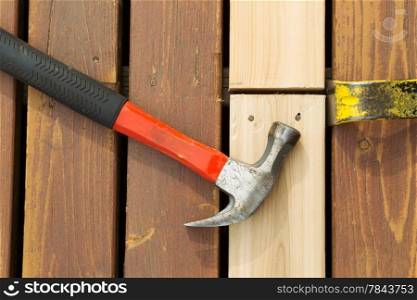Horizontal photo of used hammer and pry bar aligning new boards for installing on cedar deck