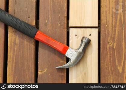 Horizontal photo of used hammer on top of newly installed cedar board next to aging deck boards