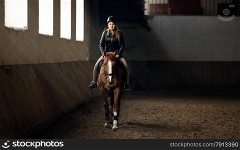 Horizontal photo of woman riding horse on manege in riding hall