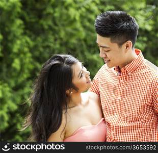 Horizontal photo of young Adult couple looking at each other with blurred green trees during daylight in background