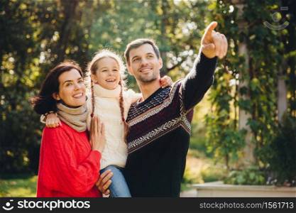 Horizontal portrait of affectionate family spend free time together, enjoy calm atmosphere. Affectionate parents play with their small child, spend weekend in open air. Relationship concept.