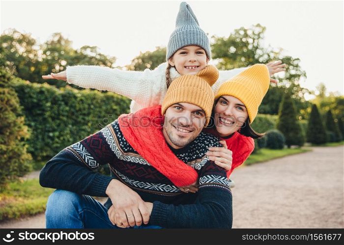 Horizontal portrait of family members spend free time together, embrace, encourage each other, have fun. Little smiling girl feels happiness, embrace her affectionate parents. Active lifestyle concept