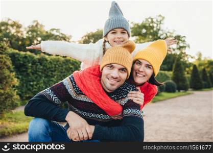 Horizontal portrait of family members spend free time together, embrace, encourage each other, have fun. Little smiling girl feels happiness, embrace her affectionate parents. Active lifestyle concept