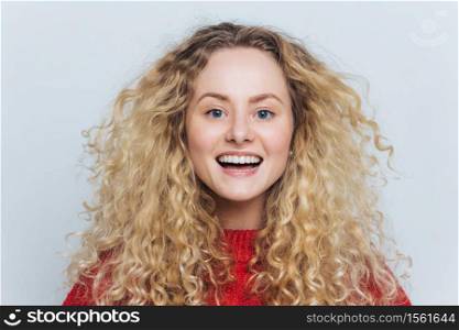 Horizontal portrait of happy adorable glad female with appealing look, feels excited as hears funny interesting story, isolated over white background. Smiling delighted woman with curly hairstyle