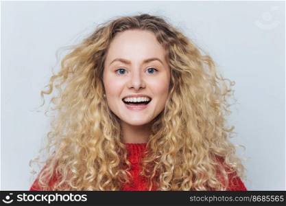Horizontal portrait of happy adorable glad female with appealing look, feels excited as hears funny interesting story, isolated over white background. Smiling delighted woman with curly hairstyle