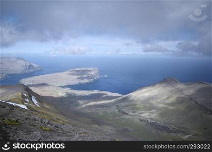 Horizontal scenery image of Faroese landscape with beautiful valley and view to the North Atlantic Ocean covered by dark clouds. Glorious sceneries of the Faroes. Postcard motif.