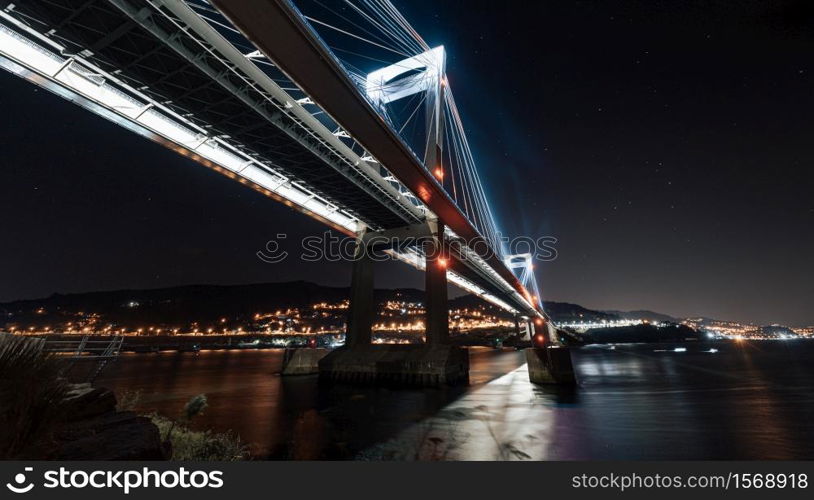 Horizontal shot of a luminous bridge from below reflecting in the water at night