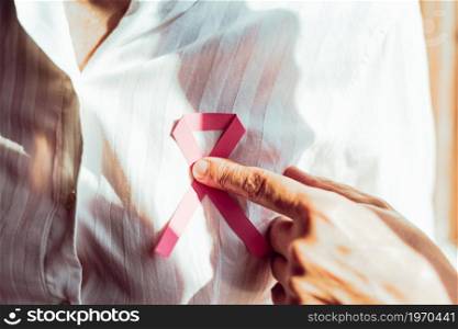 Horizontal shot of a old woman pointing pink ribbon on chest