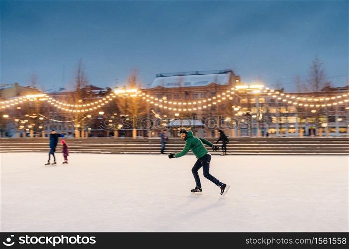 Horizontal shot of active man uses ice skates for going in for sport on ice ring, spends winter holidays actively, demonstrates professionalism and speed. Male ice skating outdoors