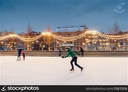 Horizontal shot of active man uses ice skates for going in for sport on ice ring, spends winter holidays actively, demonstrates professionalism and speed. Male ice skating outdoors